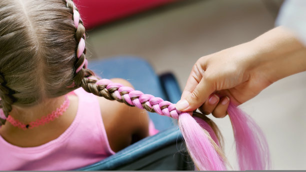 漂亮的金发女孩，七岁，扎着两条辫子，在美容院，一个发型师的沙龙，在一面大镜子前，梳着粉红色的头发。小公主图片下载