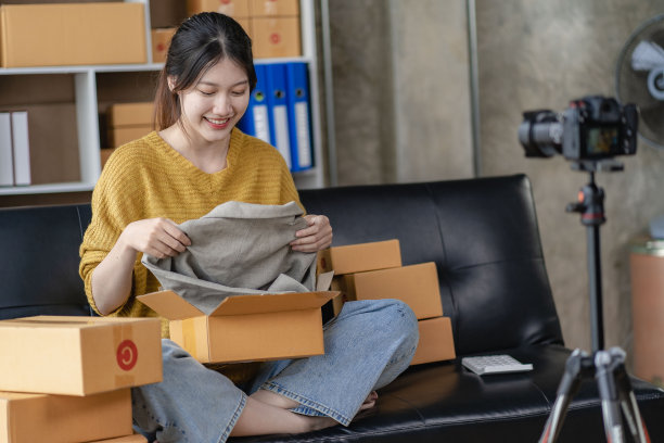 亚洲妇女坐在家里的沙发上自由职业者使用笔记本电脑与盒子，成功的亚洲妇女举手，在线营销包装和送货盒，中小企业的概念图片下载