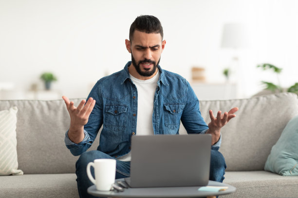 不开心的阿拉伯男子在笔记本电脑上进行视频聊天，在线讨论工作问题，坐在家里的沙发上图片下载