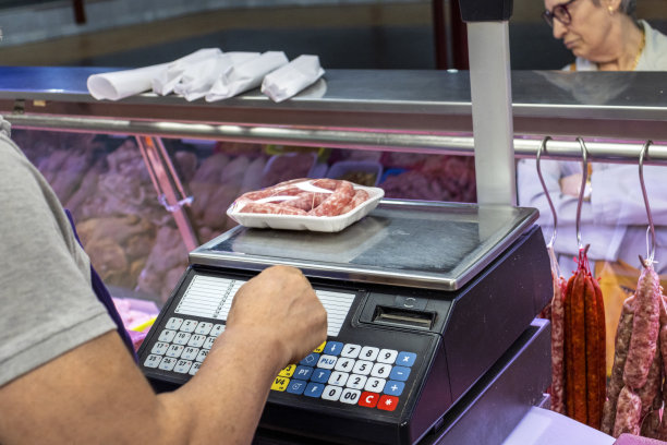 屠夫在秤上称一盘香肠的重量。销售的概念。图片下载