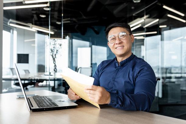 现代写字楼内成功商人画像，亚洲男子在信封里收到了好消息，打开信高兴地微笑着，看着相机图片下载