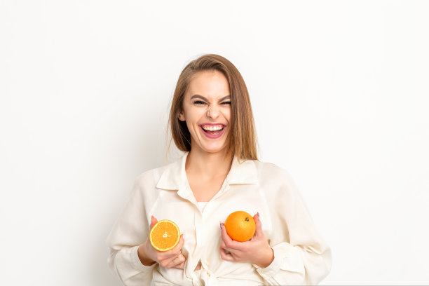 年轻的白人妇女微笑着在孤立的白色背景下拿着橘片，胸部健康的概念。图片下载