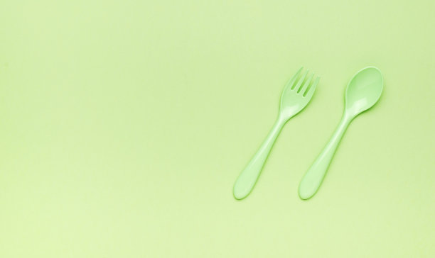 叉子和勺子是用绿色塑料做的，背景很亮。给你的短信留个地方。平的。图片下载