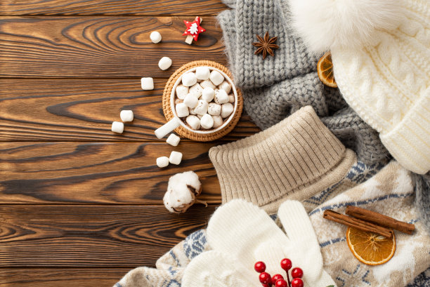 顶视图照片毛衣头饰格纹手套可可杯棉花糖在藤垫棉花花干橙片荚荚莓肉桂棒和八角在木制书桌背景图片下载