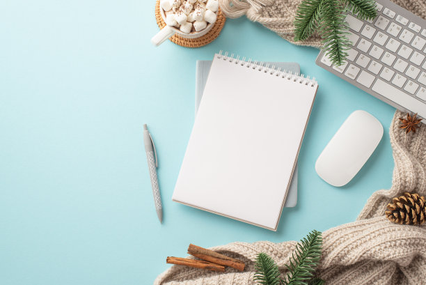 俯视图照片的工作场所键盘电脑鼠标记事本钢笔杯可可棉花糖针织格纹云杉树枝松果肉桂棒孤立的柔和的蓝色背景与copyspace图片下载