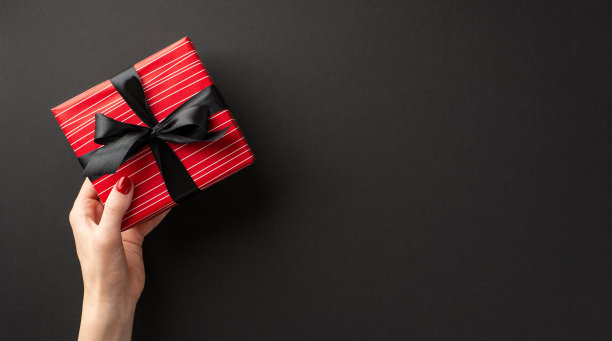 “黑色星期五”的概念。第一人称俯视图照片的女孩的手给红色礼盒与缎带蝴蝶结孤立的黑色背景与空白图片下载