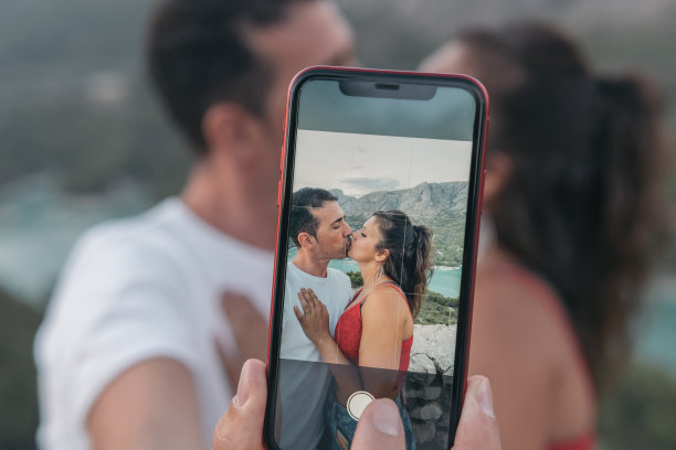 手机上的特写图片显示一对年轻的情侣，一个男孩和一个女孩在自拍，深情地接吻。图片下载