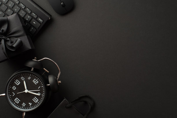 “黑色星期五”的概念。顶视图照片黑色闹钟礼盒丝带蝴蝶结纸袋电脑鼠标和键盘上孤立的黑色背景与copyspace图片下载