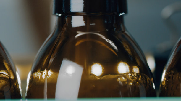 在工厂的生产线上，一排玻璃瓶被推上来，装满液体剂。制药行业医疗用品用药品的生产。自动装瓶线。近距离图片下载