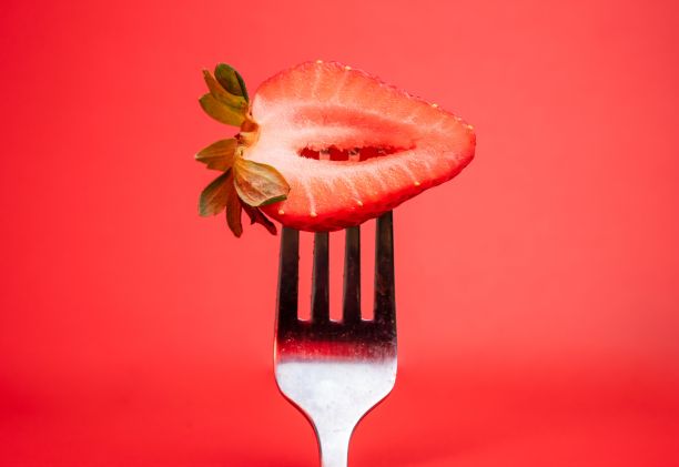 红色背景上有半个草莓的叉子的特写镜头图片下载