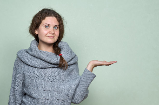 卷发、穿毛衣的漂亮女人用手指了指。照片在绿色背景与复制空间图片下载