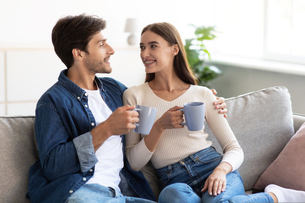 幸福微笑的年轻欧洲夫妇坐在沙发上，喝着最爱的饮料，交流着图片下载