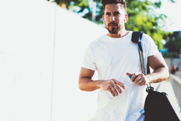 白人健美运动员与包和水瓶清新的收听音频播客与运动信息，肌肉发达的男性跑步者在电子耳机走在城市设置在城市图片下载