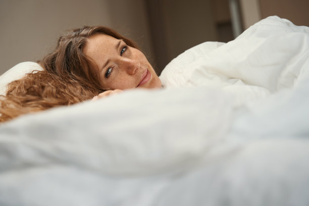 女人躺在卧室的床上，盖着温暖的毯子图片下载