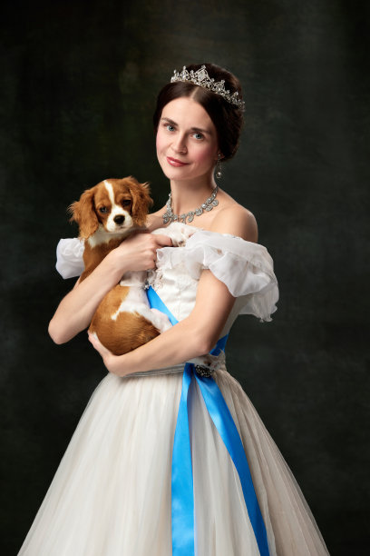 心爱的宠物。肖像年轻迷人的女人在白色古着中世纪公主抱着小国王查尔斯猎犬在黑暗的背景。图片下载