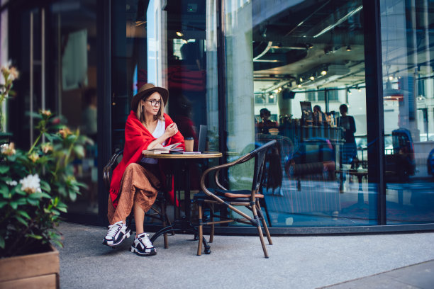 时髦的年轻女子戴着帽子，坐在寒冷的咖啡馆露台上看书图片下载