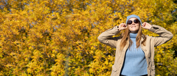 在秋天的公园里，戴着墨镜微笑的年轻女子。温暖的阳光明媚的天气。秋天的概念图片下载