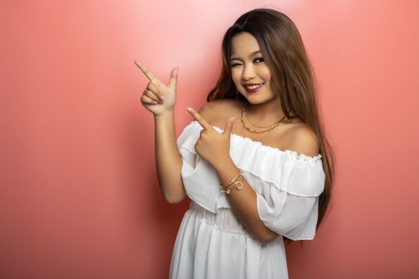 迷人的年轻菲律宾女子眨眼，指着一堵粉红色的墙图片下载