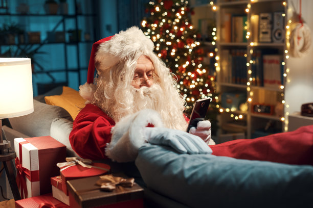 圣诞老人坐在沙发上玩智能手机图片下载