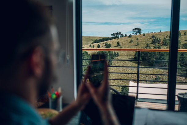 一个男人在家里工作，用他的智能手机拍照的后视图图片下载