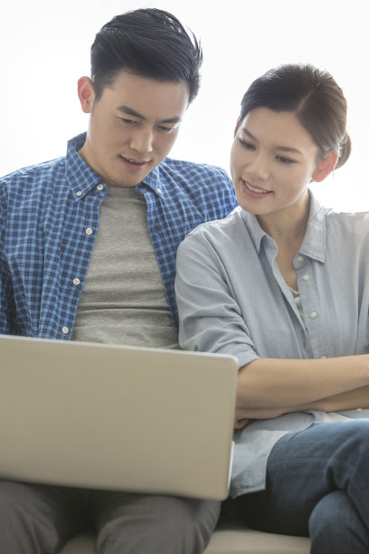 年轻夫妇在沙发上放松和使用他们的笔记本电脑，着迷于产品介绍页面-库存照片图片下载