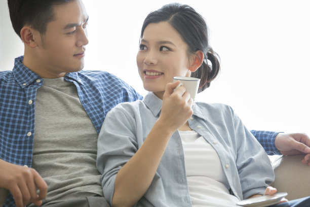 年轻的夫妇在沙发上休息，丈夫为他月经来的妻子准备热饮-库存照片图片下载