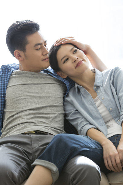 年轻夫妇在新家的沙发上享受生活，妻子依偎在丈夫的怀里，表情充满了渴望和期待——库存照片图片下载