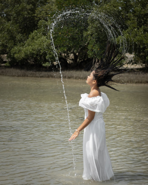 东南亚湿女孩在白色的裙子赤脚站在海洋做水喷雾图片下载