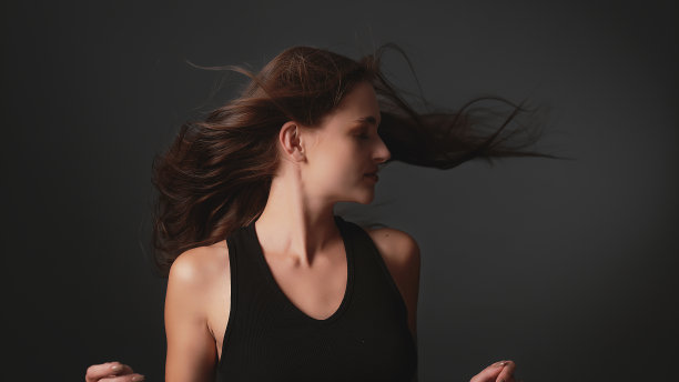 美丽的，诱人的褐发女人在黑暗的背景。光泽的棕色健康的头发在风中摇曳。图片下载