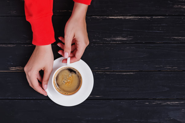 女人的手在红色运动衫拿着一杯新鲜的热咖啡，俯视图片下载