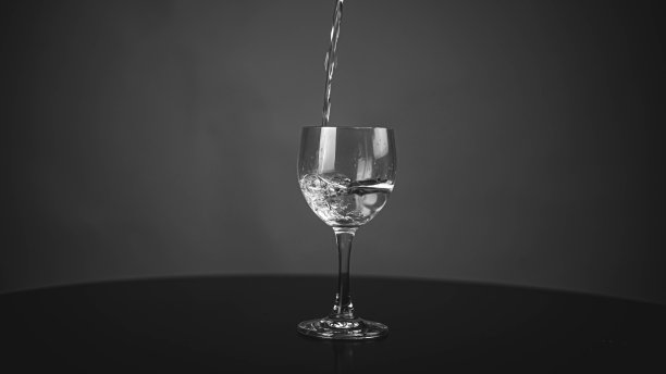 将纯净的饮用水倒入玻璃杯中。水杯:灰色背景上有水的玻璃杯图片下载