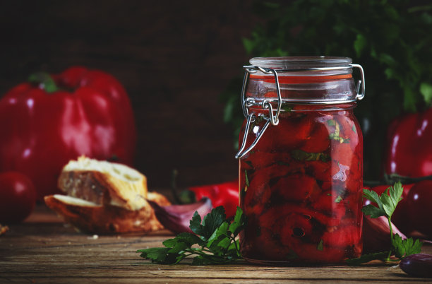 烤红辣椒罐头，与辣椒，大蒜和香草腌制玻璃罐中。质朴的木质厨房餐桌背景图片下载