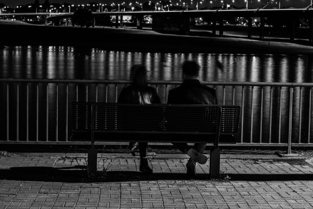 一对夫妇坐在长凳上看夜晚的河流的灰度照片图片下载