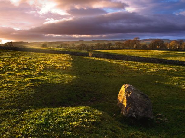 秋天，厚厚的云层覆盖在长满草和岩石的山丘和农村的农田上图片下载