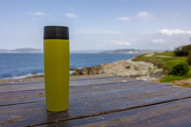 靠近大海的木桌上放着一个绿色保温杯。图片下载