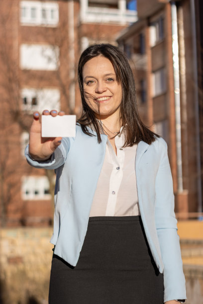 身穿蓝色夹克的微笑女商人在户外展示名片。垂直的肖像。名片图片下载