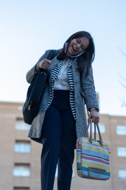 年轻女子一边拿着包，一边用耳朵和肩膀夹着电话说话图片下载