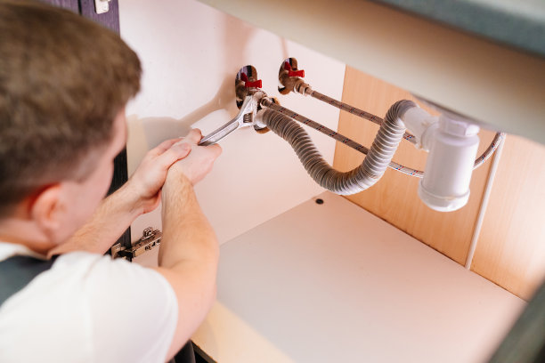 一名男水管工正在修理浴室水槽下的虹吸。图片下载