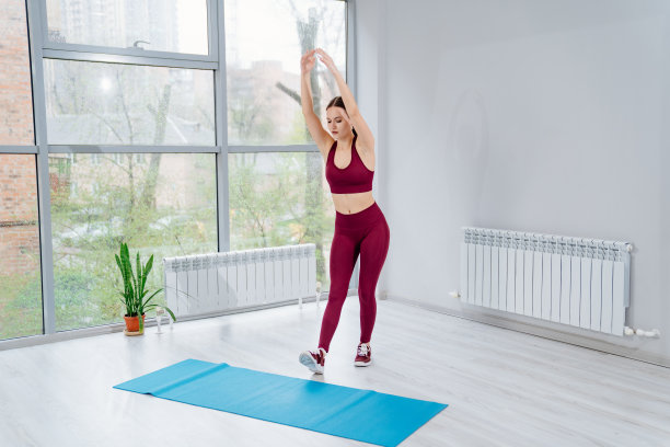 一个穿着酒红色运动服的女人在健身房锻炼。热身和拉伸。图片下载