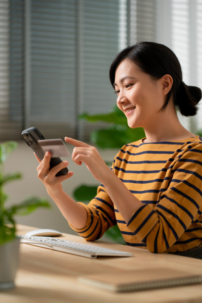 亚洲妇女拿着信用卡，用智能手机在家办公室网上购物。图片下载