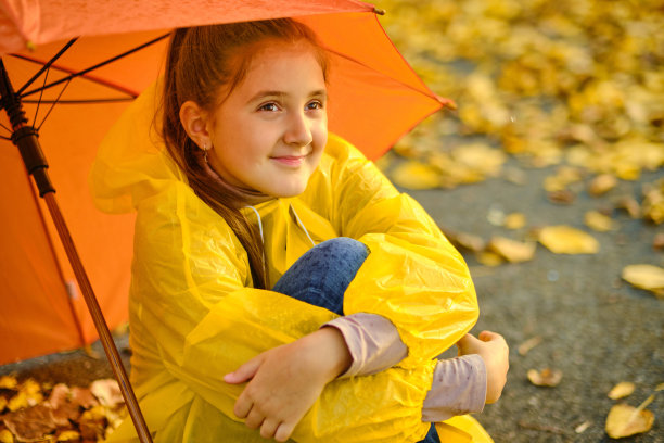 雨中，女孩坐在柏油路上，撑着一把橙色的雨伞图片下载