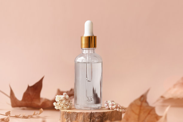 透明玻璃化妆品滴管瓶站在木圆盘与干花和叶子。秋天的成分图片下载