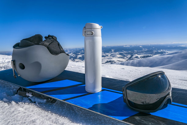 雪山顶上滑雪板上的滑雪头盔、保温瓶和护目镜图片下载