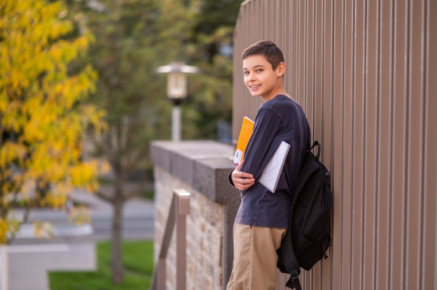 一个微笑着靠在波纹金属栅栏上的学生图片下载