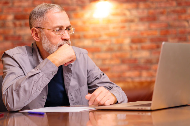 戴着眼镜的中年老人微笑着在家里用笔记本电脑工作图片下载