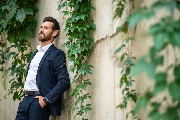 一个穿着雅致西装的年轻人站在墙边图片下载