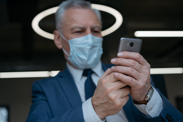 男子戴着医用口罩使用手机、通讯、上网工作，专注于双手。冠状病毒，社会距离的概念图片下载