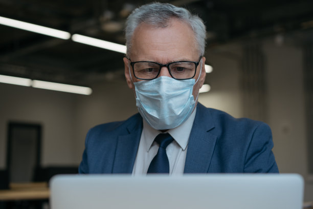 戴着医用口罩的男子使用笔记本电脑，交流，上网，在家工作图片下载