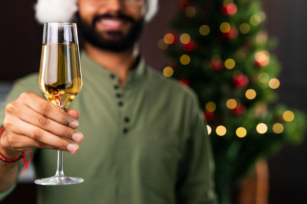 印度男子在家里喝着酒，圣诞树上装饰着花环图片下载