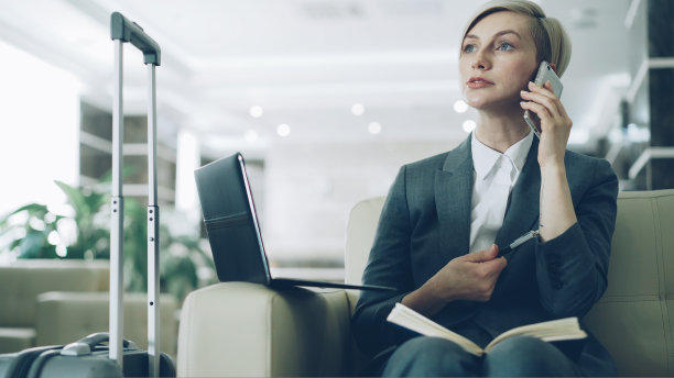 金发忙碌的女商人坐在酒店大厅的扶手椅上讲手机，在记事本上写东西，使用笔记本电脑。商务，旅行和人的概念图片下载